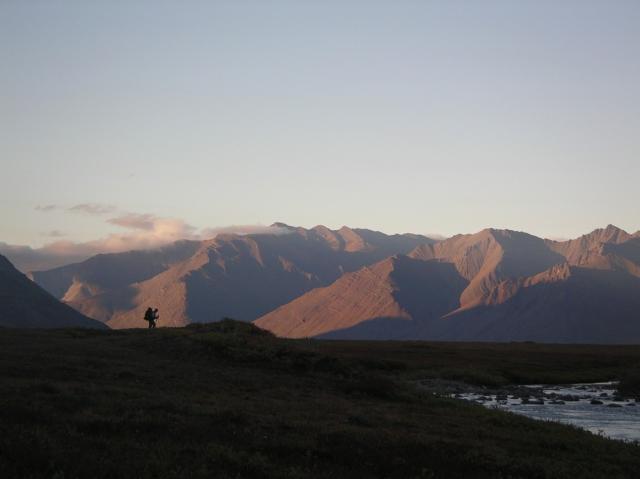 A tiny silhouette of a lone hiker is dwarfed by immense rivers and mountains