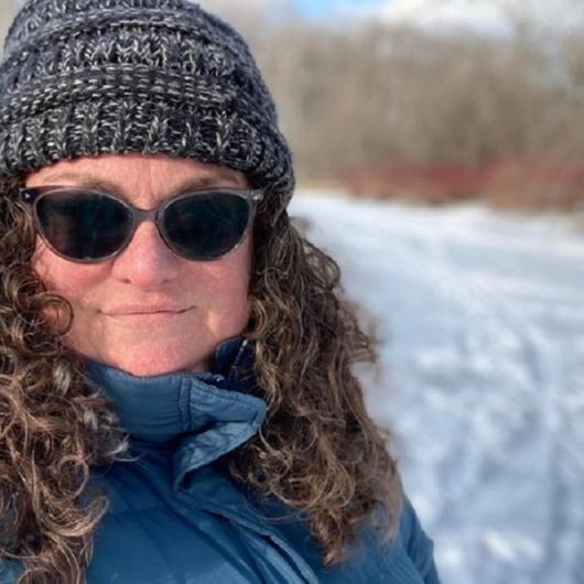 A woman wearing a winter hat. Snowy field is in the background. 