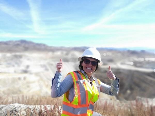A woman wearing a reflector vest and a hard hat gives the thumbs up