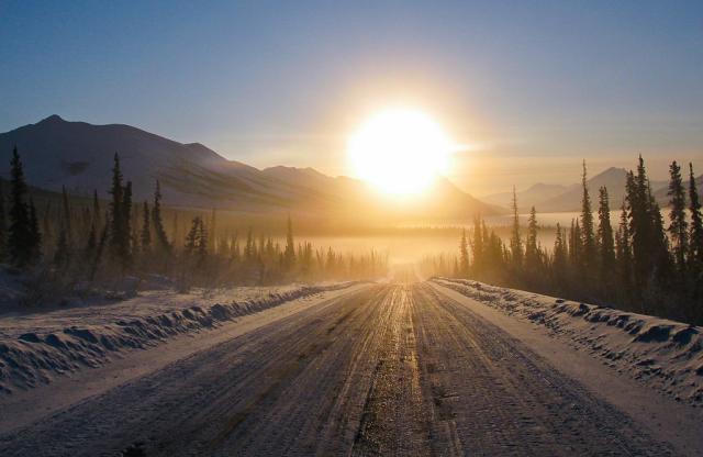 The winter sun hangs over the horizon, casting a glare on the icy Dalton Highway.