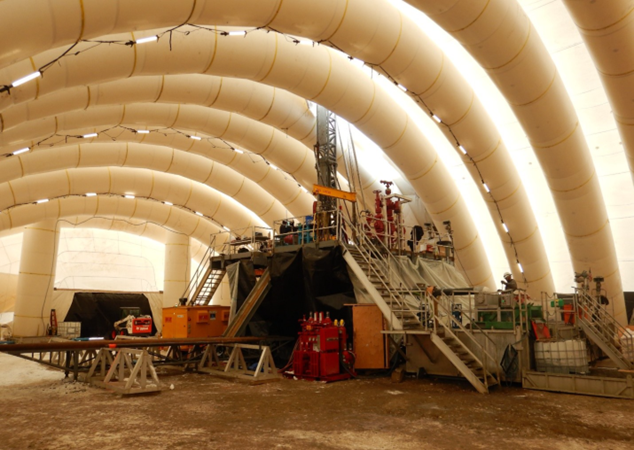 Inside of a large dome, dirt floor, oil rig nearby.