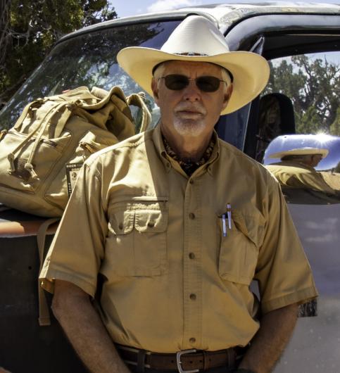 Man in a tan shirt wearing sunglasses and a large hat with upturned brim