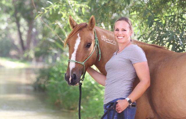 Woman stands next to horse. 