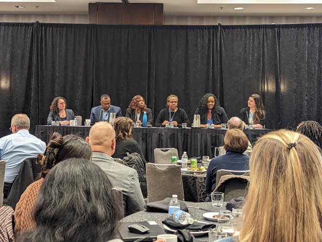 Panel of speakers facing an audience seated at tables