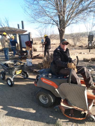 man wearing a cap on a riding lawnmower pulling a small wagon 