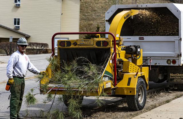 A man chips branches and logs using a chipper machine.