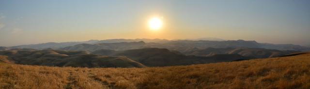 Dry grassy hills with the sun in the background