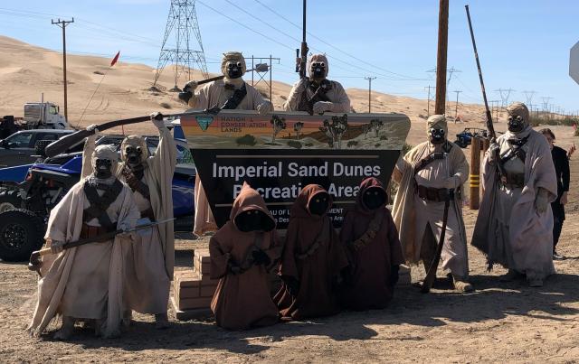 Several people in star wars costumes next to a sign for the Imperial Sand Dunes Recreation Area.