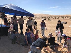 Children digging in sand under a tent in the desert.
