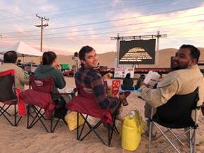 People sitting in camp chairs watching a movie in the desert.