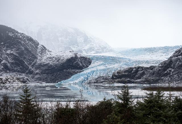 A glacier behind glacial lake between tree-filled mountains