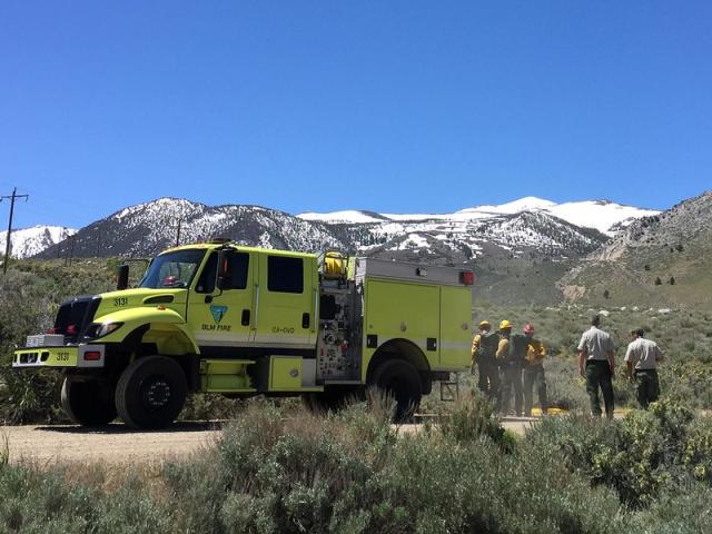 A yellow fire engine and firefighters standing next to it.