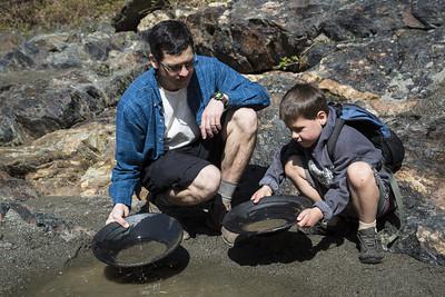 A Father and sun gold pan next to a forest river.