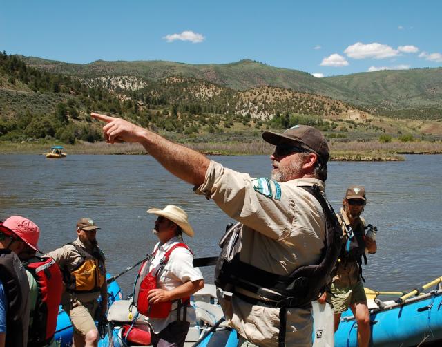 BLM employee pointing in the distance with the Colorado River and four other people in the background of the image. 