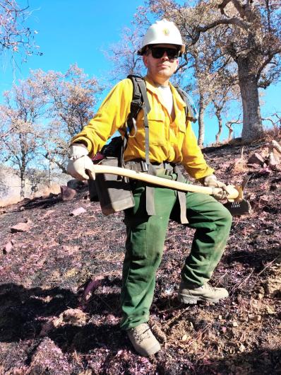 A firefighter standing on a hillside holding a pulaski.