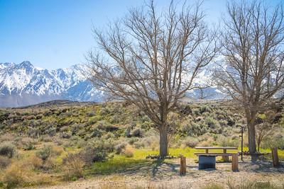 A picnic table and fire ring with tall snow peaked mountains in the background. 