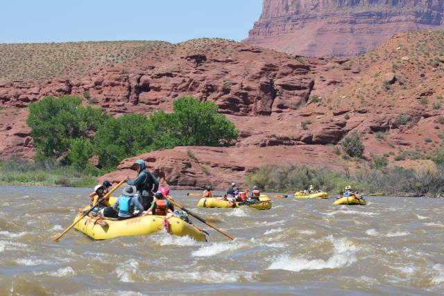 Yellow rafts with youth going through rapids on a river.