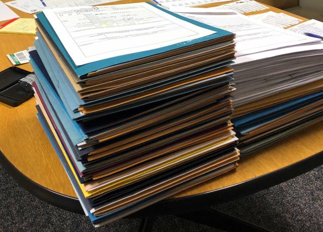 A stack of folders and paperwork sit side by side on a table.