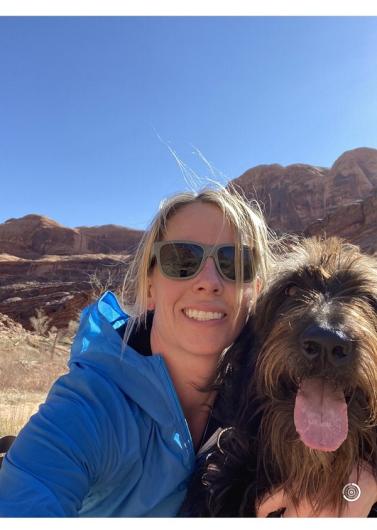 A woman with a brown dog. Red rocks are in the background. 