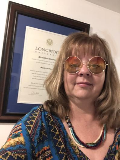 A woman is standing in front of a document in a frame that is hanging on the wall.