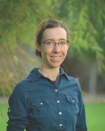 A woman wearing a blue shirt with green trees in the background