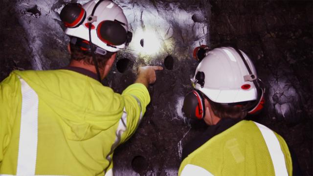 Workers in a mine peruse a rock wall. 