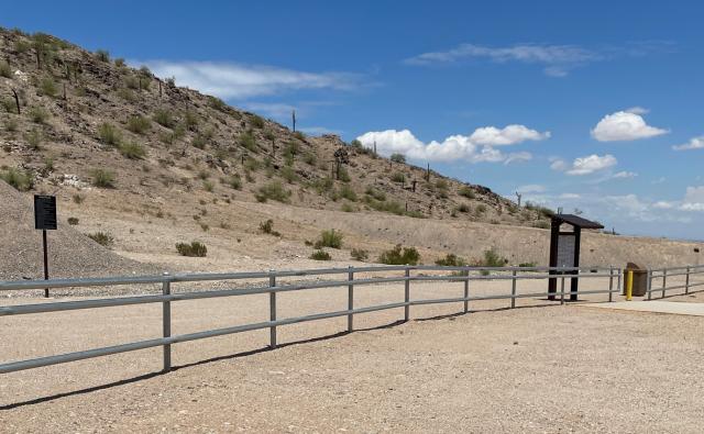 in a desert landscape a pipe-rail fence with signs and kiosks