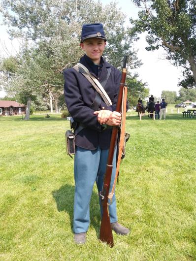 A boy stands in period military soldier uniform holding a rifle. 