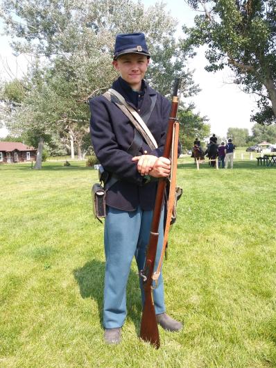 A boy stands in period military soldier uniform holding a rifle.
