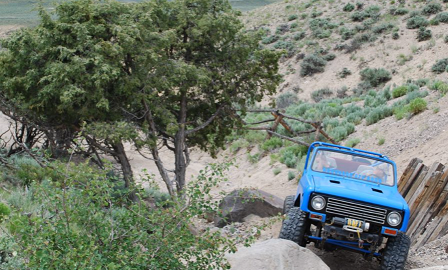 A blue jeep riding over large rocks. 