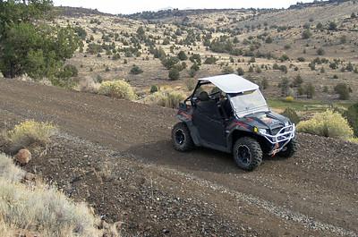 A UTV travels a dirt road in the high desert.