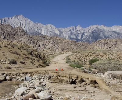 A washed out road with a tall snow capped mountain in the background.