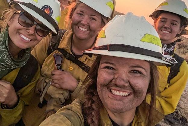 Four firefighter covered in soot and dirt smile at the camera