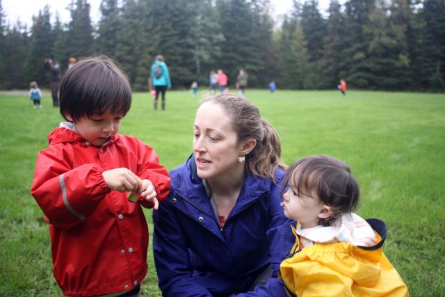 A caregiver and two small children enjoy curious explorations of a soggy mushroom.