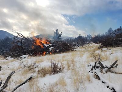 Pile of brush burns in snowy field.