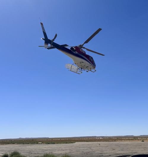 A helicopter flying over ground with clear blue skies.