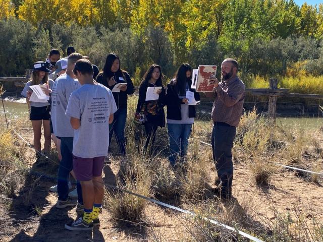 A group of students stands together looking at a document out on the landscape. 