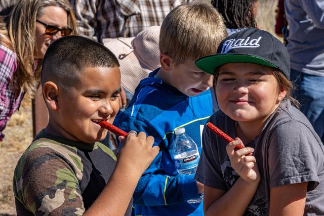 A group of three students with two of them eating beef jerky sticks and smiling