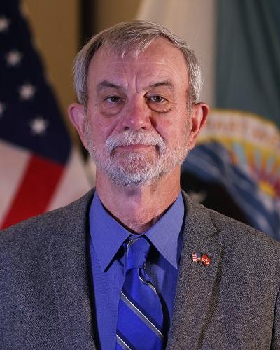 person with short hair wearing a tie posing in front of the American flag