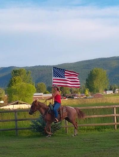Woman riding horse with an American flag along a fence line