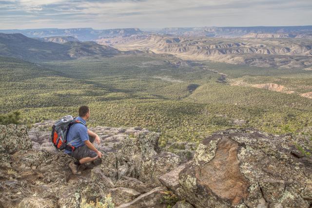 A hiker kneels on a cliff edge overlooking the Grand Canyon-Parashant National Monument.