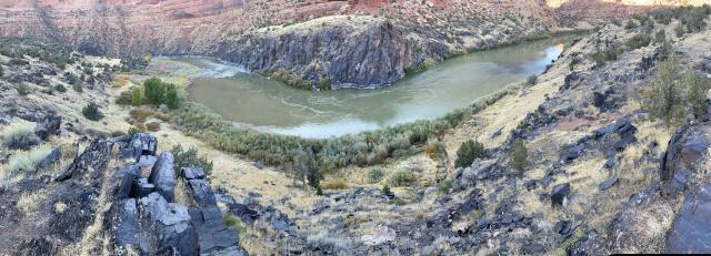 A panoramic view of the Colorado River making its way through Westwater Canyon. Heavy green growth is along part of the shoreline.