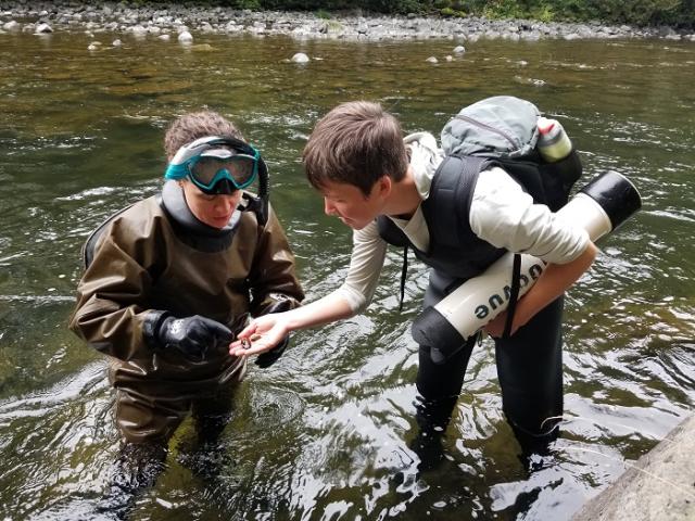 two scientists wearing goggles standing in a river holding equipment