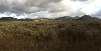 A high desert meadow during a rain storm with mountains in the background.