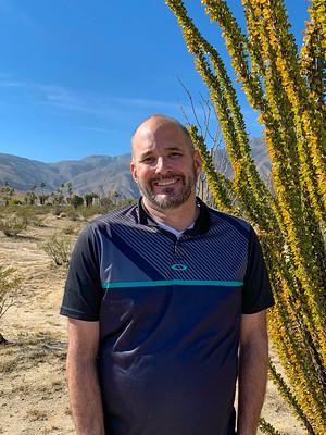 Matt Lohr stands in front of a cactus with desert mountains in the background.