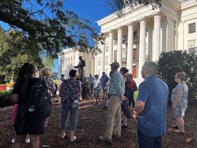 The picture shows individuals in front of the Alabama State Capitol.