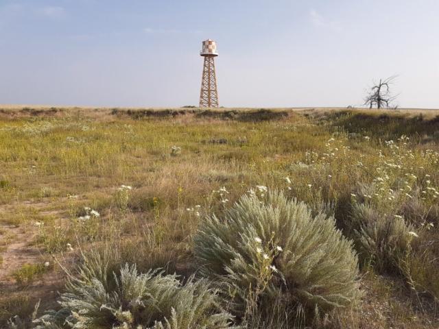 An orange and white color painted water tower sits on the horizon of the lush green Colorado prairie at the site of the former Granada Relocation Center.