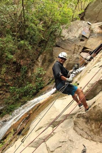 Carlos Joya, who is wearing shorts and safety gear, rappels down a cliff face.