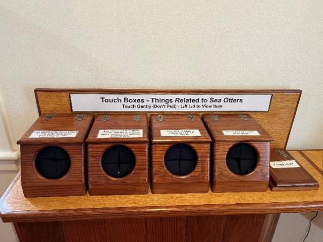 Photo shows 4 wooden boxes with holes cut in the front so visitors can put their hand in the box to feel what’s inside.