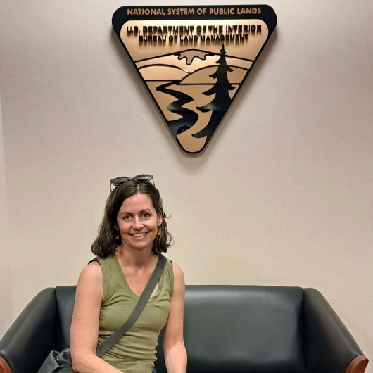 Tiffany Shepherd sits on a couch in front of a Bureau of Land Management logo wall placard.